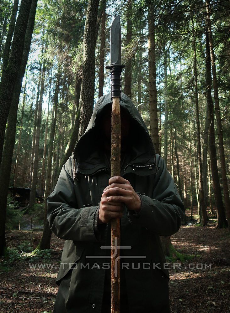 Kovaný nůž pro survival nasazený na dřevěné tyči jako improvizované kopí nebo oštěp v lese.