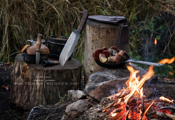 KNIVES by Tomas Rucker Large Bowie knife and small mushroom knife by a campfire with a frying pan.