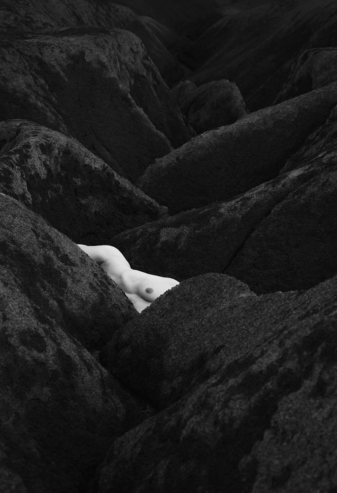A captivating monochrome artistic photograph by Tomas Rucker showcasing a seamless integration of soft human curves with the rugged, dark textures of a rocky landscape, emphasizing the harmony between organic form and natural geometry.