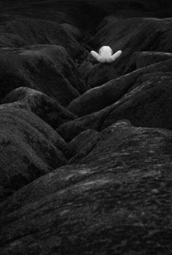 Symbiosis of organic curves and rugged geological structures Fine art monochrome composition exploring the concept of organic integration. A smooth, curved human form is nestled within a deep, dark rocky valley, creating a contrast between soft skin and textured stone.